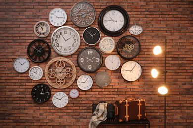 Photo of Collection of clocks hanging on red brick wall indoors