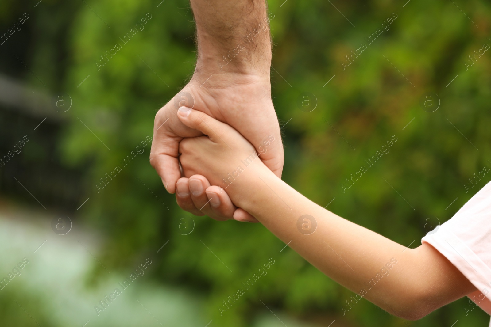 Photo of Man and child holding hands outdoors, closeup