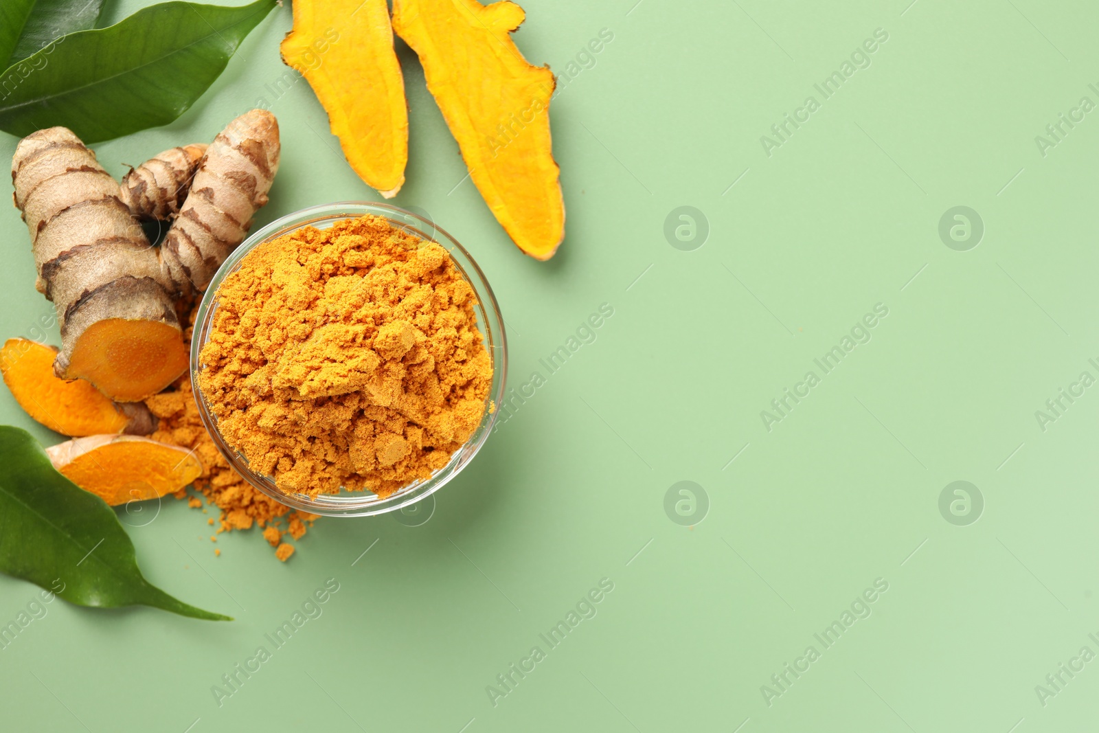 Photo of Aromatic turmeric powder, raw roots and leaves on green background, flat lay. Space for text