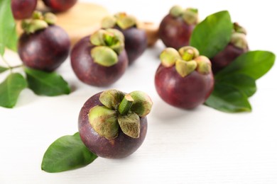 Photo of Fresh ripe mangosteen fruits with green leaves on white table