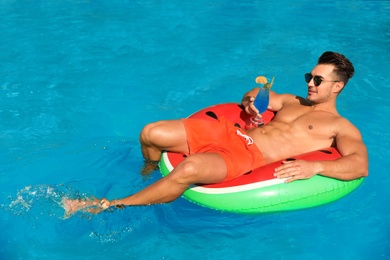 Young man with cocktail and inflatable ring in pool on sunny day