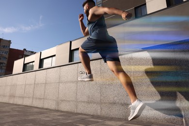Image of Sporty young man running on street, low angle view. Light trails showing his speed