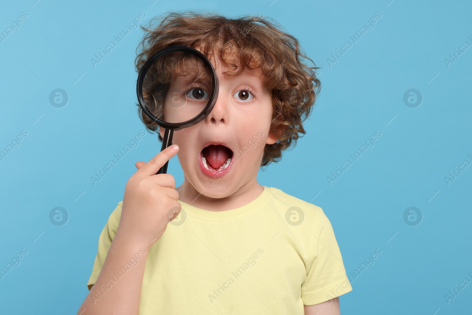 Photo of Cute little boy looking through magnifier glass on light blue background