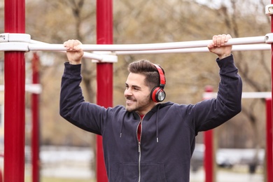 Photo of Young man with headphones listening to music and exercising on sports ground