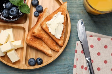 Photo of Tasty toasts served with butter and blueberries on light blue wooden table, flat lay