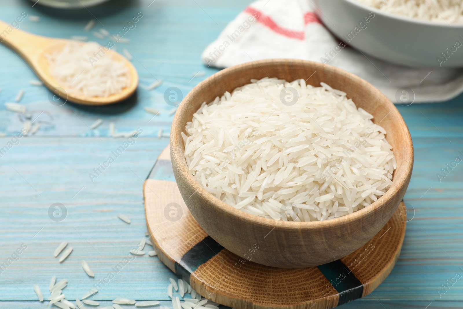 Photo of Raw basmati rice in bowl on light blue wooden table, closeup. Space for text