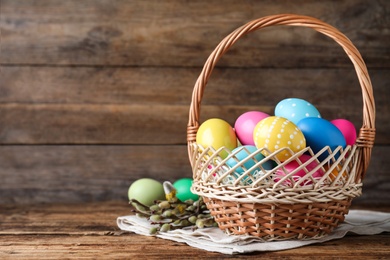 Colorful Easter eggs in wicker basket and willow branches on wooden background. Space for text