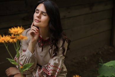 Photo of Beautiful woman wearing embroidered dress in blooming garden, space for text. Ukrainian national clothes