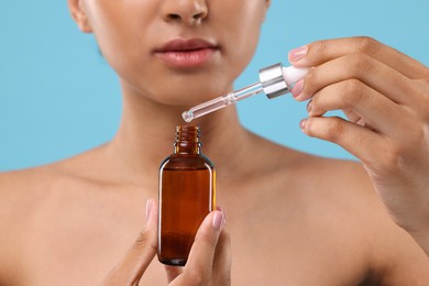 Woman with bottle of serum and dropper on light blue background, closeup