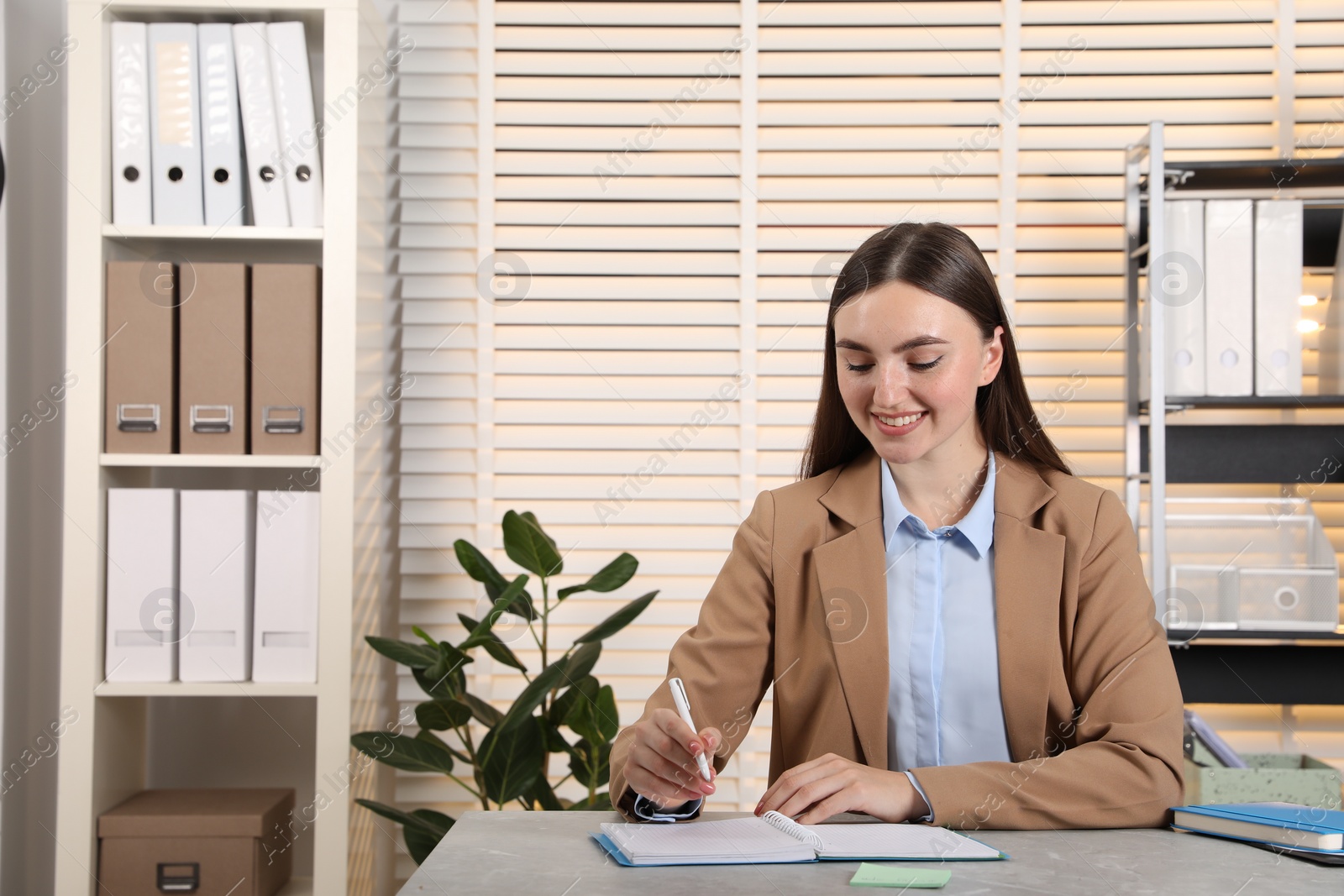 Photo of Happy woman taking notes at light grey marble table in office