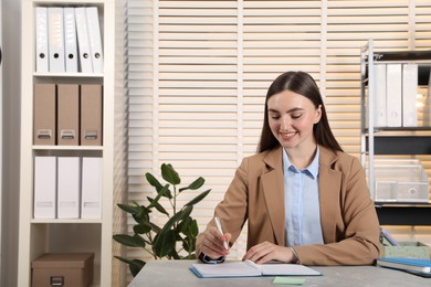 Photo of Happy woman taking notes at light grey marble table in office