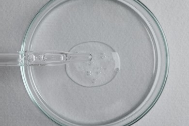 Photo of Petri dish with sample of cosmetic oil and pipette on white background, top view