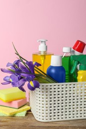 Spring cleaning. Basket with detergents, flowers and sponges on wooden table against pink background