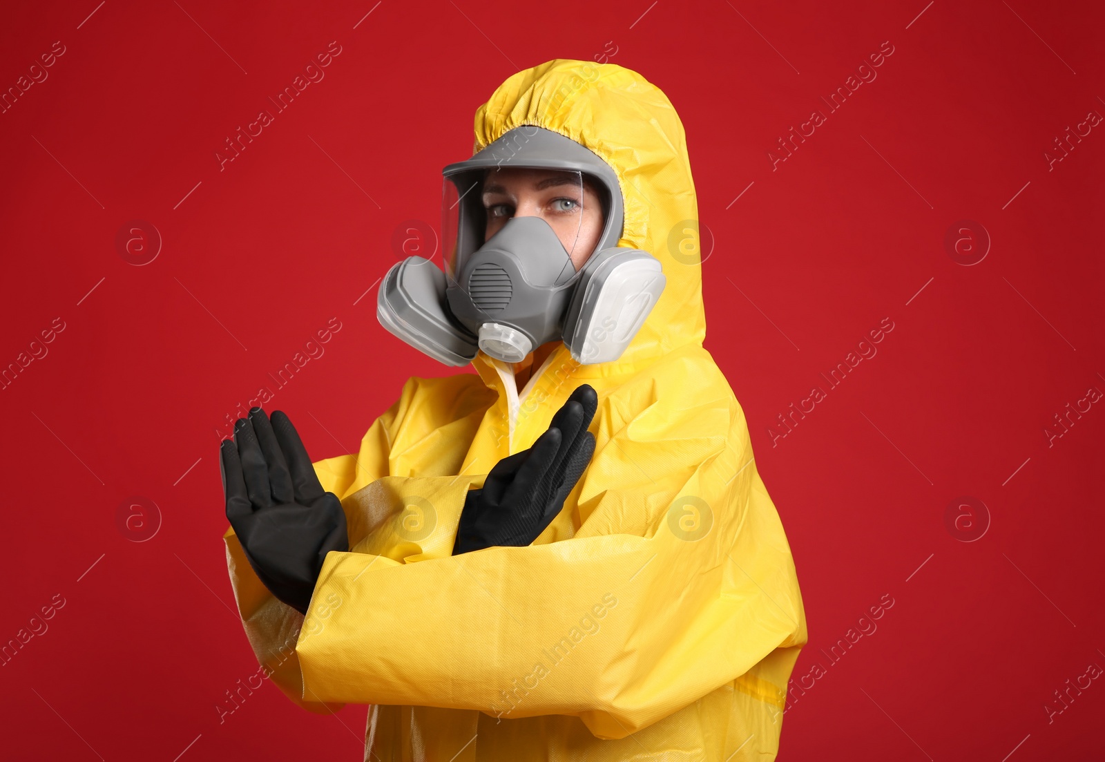 Photo of Woman in chemical protective suit making stop gesture on red background. Virus research