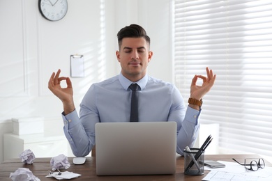 Businessman meditating at workplace in office. Stress relieving exercise