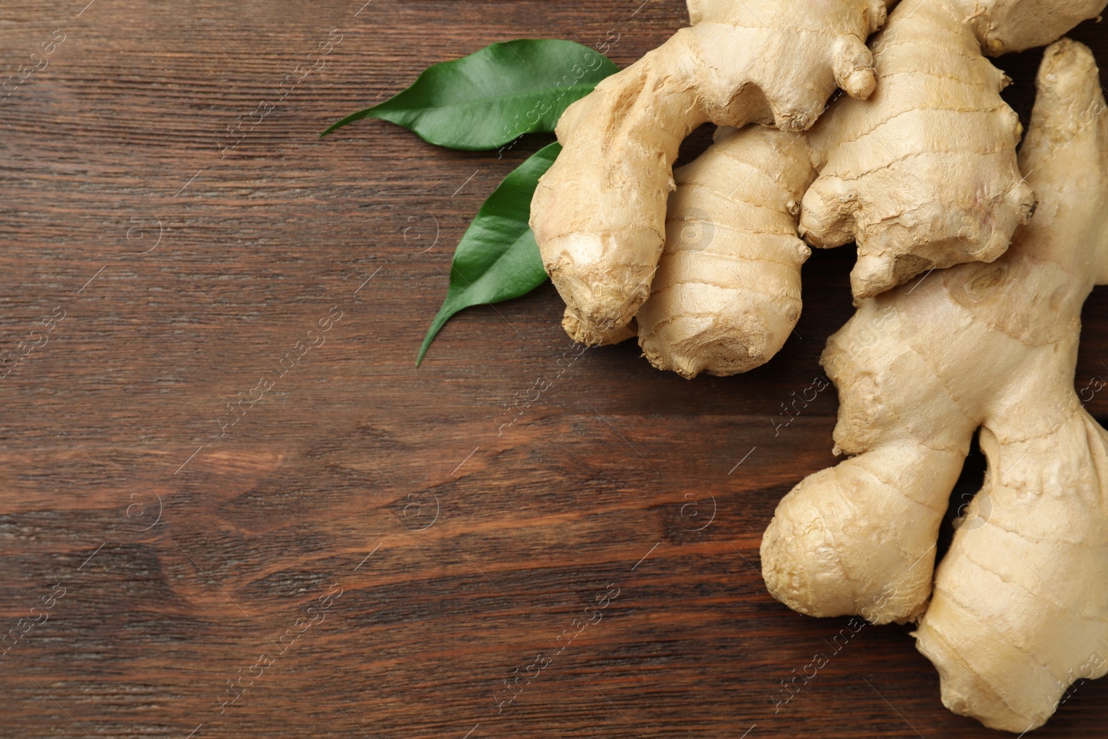 Photo of Fresh ginger with leaves on wooden table, top view. Space for text