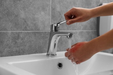 Photo of Woman holding burned hand under cold water indoors, closeup. Space for text