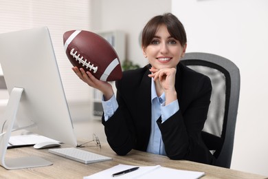 Photo of Smiling employee with american football ball at table in office