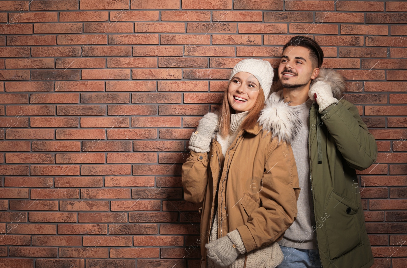 Photo of Young couple wearing warm clothes against brick wall, space for text. Ready for winter vacation