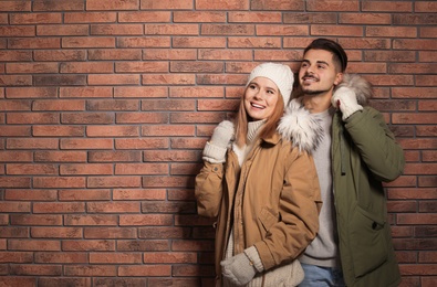 Photo of Young couple wearing warm clothes against brick wall, space for text. Ready for winter vacation