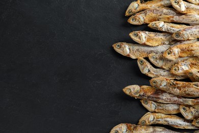 Photo of Delicious dried anchovies on black table, flat lay. Space for text