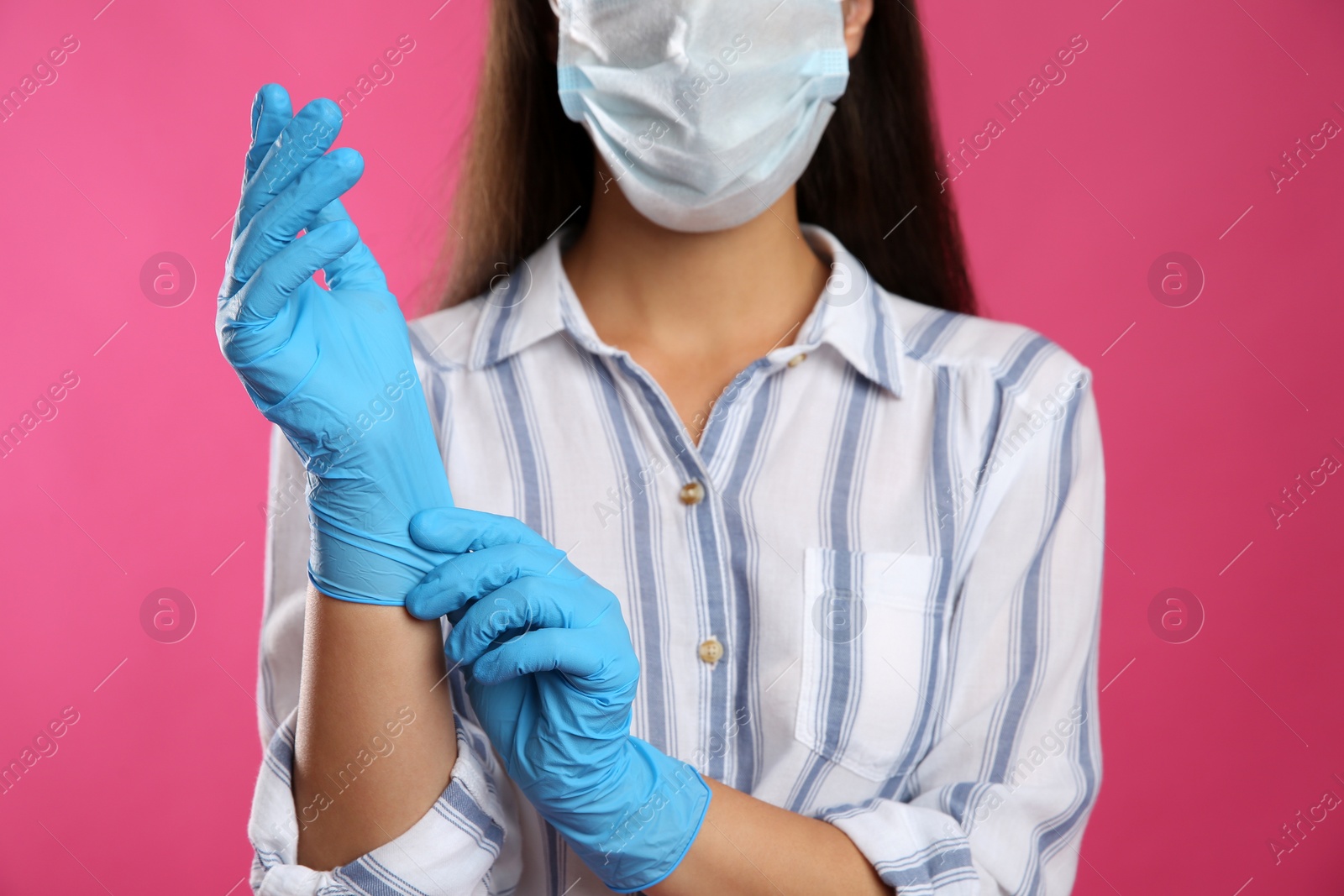 Photo of Woman in protective face mask putting on medical gloves against pink background, closeup