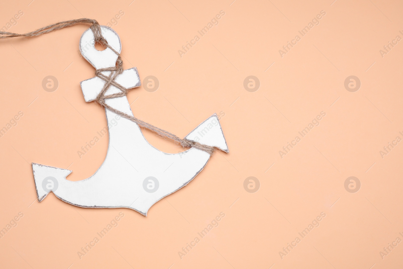 Photo of White wooden anchor figure on pale orange background, above view. Space for text