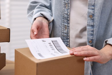 Parcel packing. Post office worker sticking barcode on box indoors, closeup