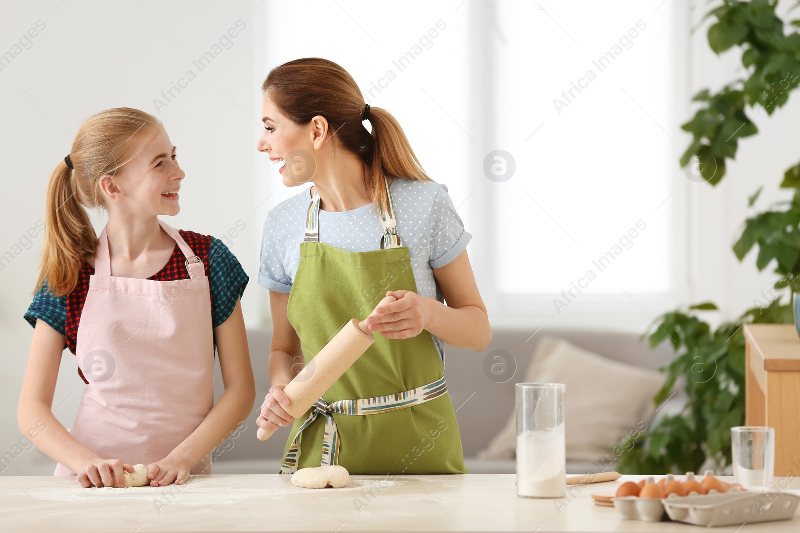 Photo of Mother and her daughter making dough at table in kitchen