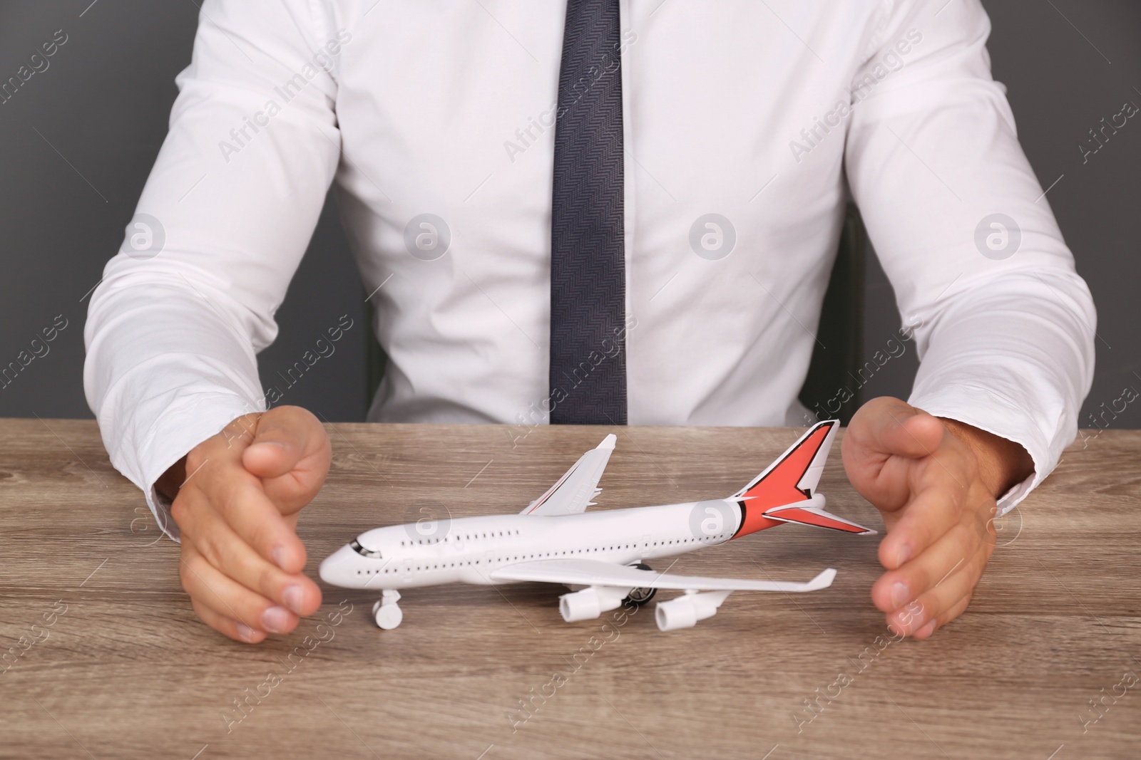 Photo of Insurance agent covering toy plane at table, closeup. Travel safety concept