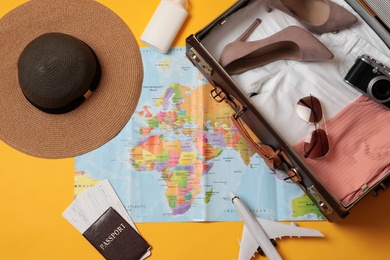 Flat lay composition with packed suitcase and travel accessories on yellow background. Summer vacation