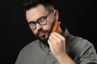 Photo of Handsome young man combing beard on black background