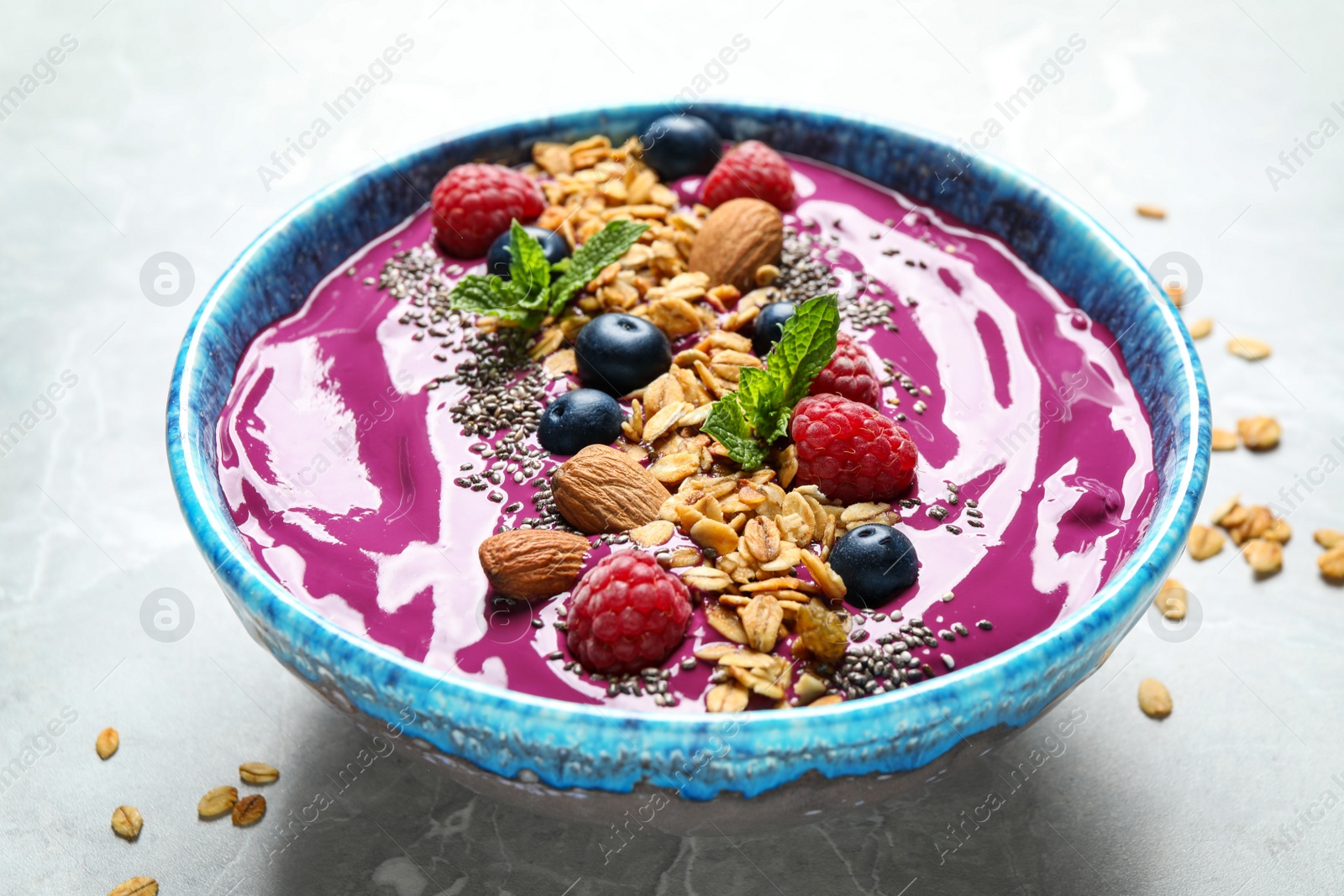 Photo of Delicious acai smoothie with granola and berries in dessert bowl on light marble table