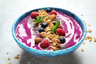 Delicious acai smoothie with granola and berries in dessert bowl on light marble table