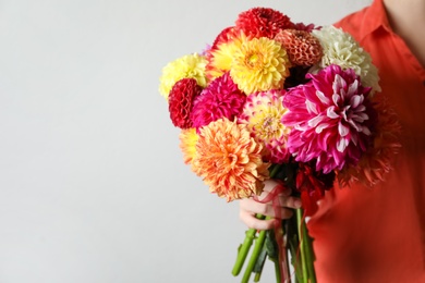 Photo of Woman with bouquet of beautiful dahlia flowers on light background, closeup. Space for text