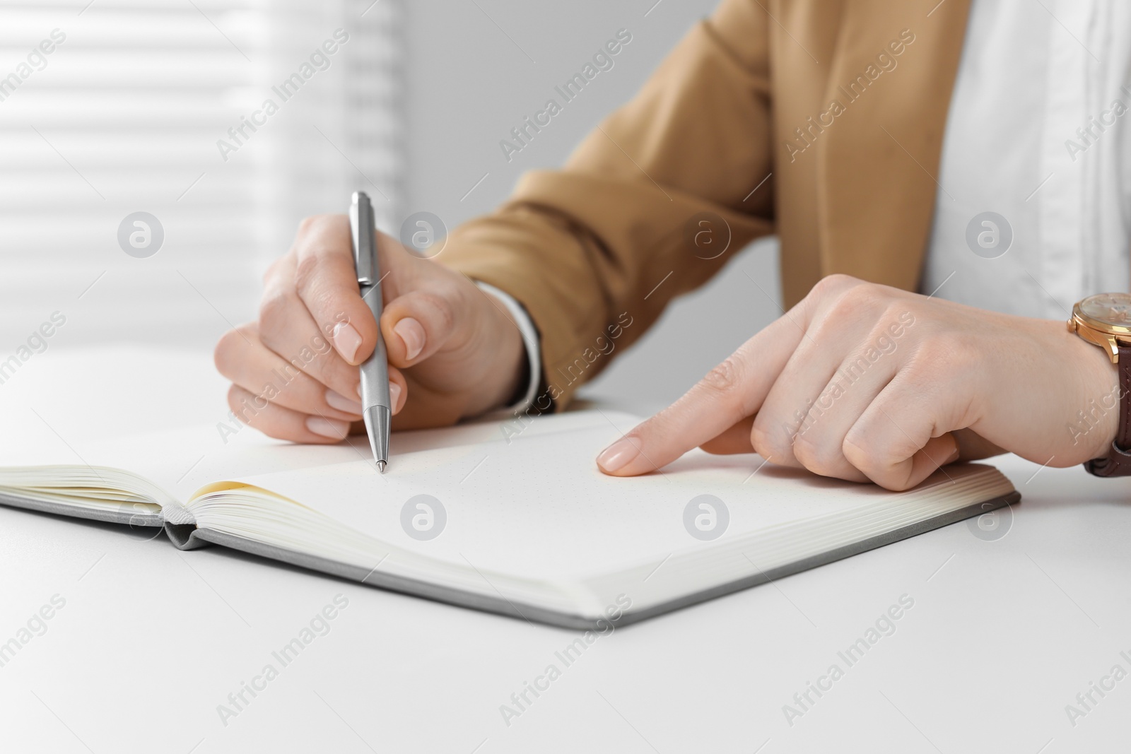 Photo of Woman writing in notebook at white table, closeup