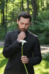 Sad man with calla lily flower outdoors. Funeral ceremony
