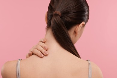 Woman touching her neck on pink background, back view