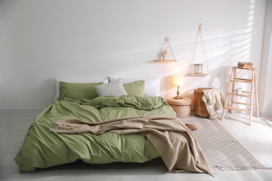 Comfortable bed with olive green linen in modern room interior