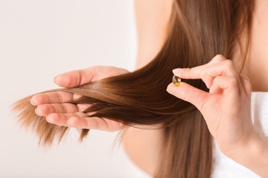 Photo of Woman holding vitamin capsule for hair health on light background, closeup