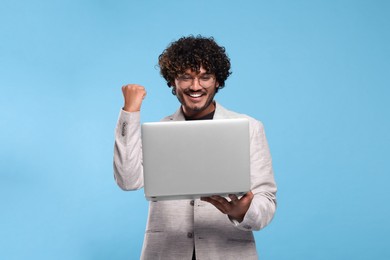 Photo of Happy man with laptop on light blue background. Space for text