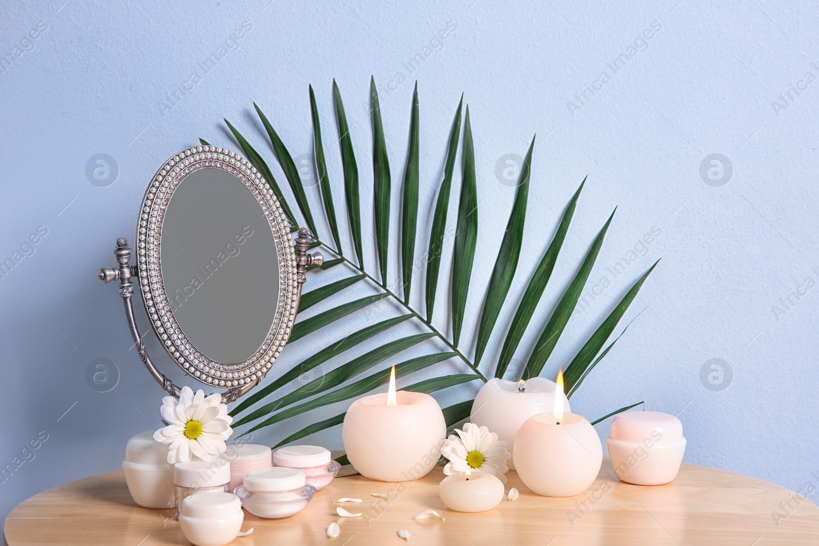 Photo of Stylish mirror, cosmetic products and aroma candles on table near light wall