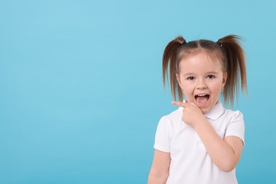 Photo of Portrait of emotional little girl pointing at something on light blue background, space for text