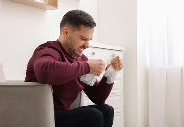 Photo of Emotional man with bubble wrap indoors. Space for text