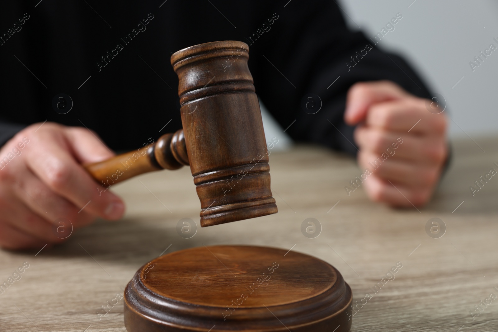 Photo of Judge with gavel sitting at wooden table against light grey background, closeup