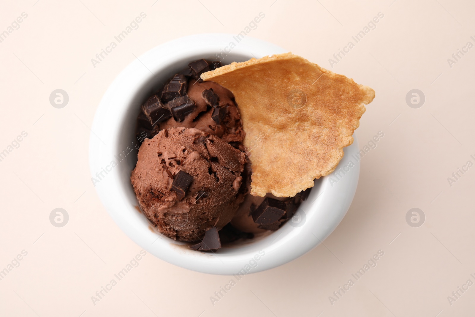 Photo of Tasty chocolate ice cream and piece of waffle cone in bowl on beige background, top view