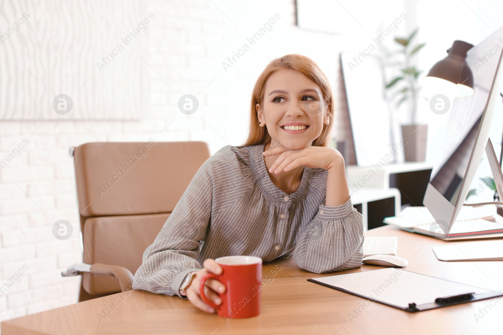 Photo of Young woman with cup of drink relaxing at table in office during break