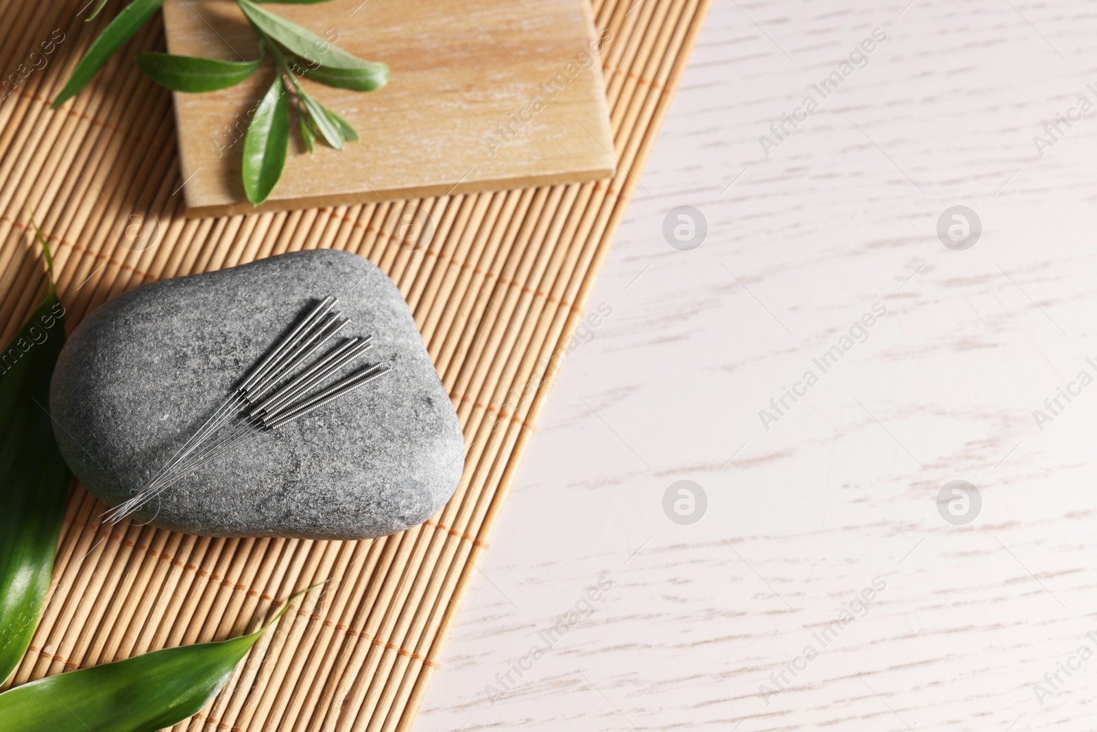 Photo of Stone with acupuncture needles and leaves on white wooden table, top view. Space for text