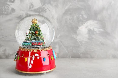 Photo of Beautiful snow globe with Christmas tree on light grey stone table. Space for text