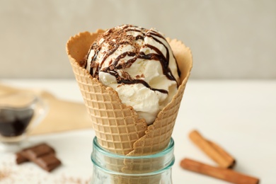 Photo of Delicious vanilla ice cream with toppings in wafer cone on white table, closeup